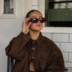 Woman wearing polarised chocolate espresso oval sunglasses and a brown jacket in an indoor setting